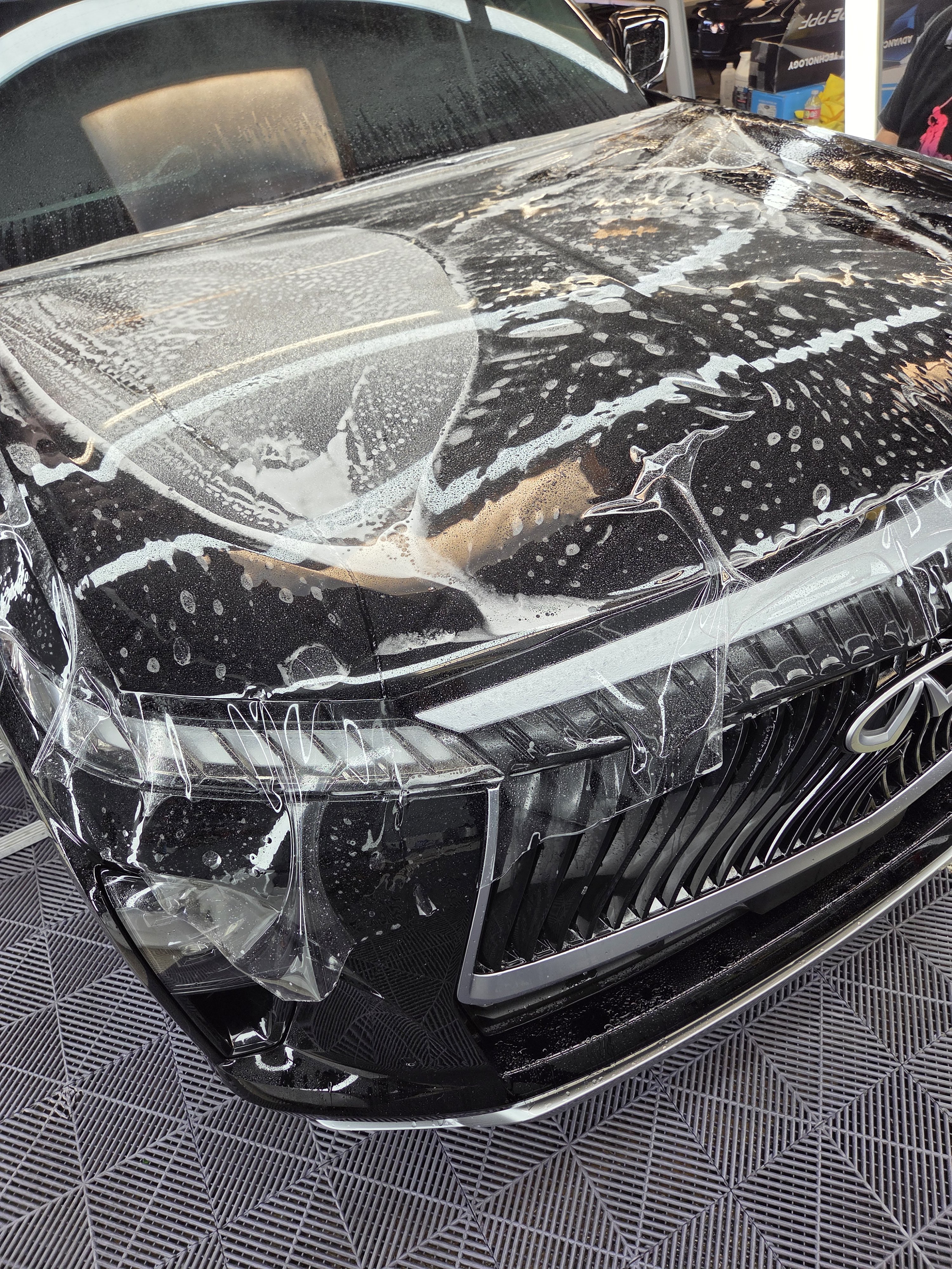 Detailer squeegeeing clear protective film across the hood of a yellow sports car
