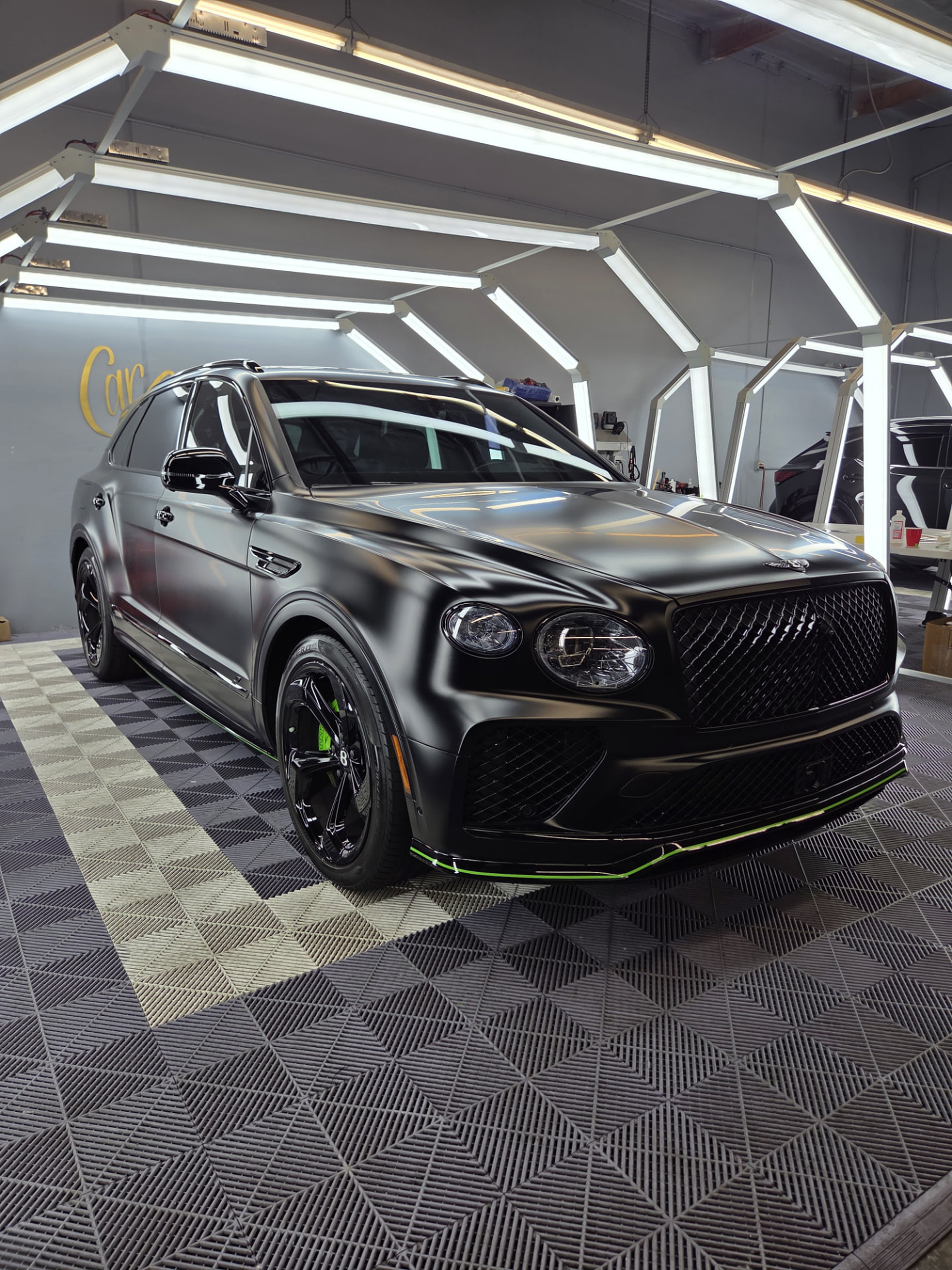 Detailer using an inspection light to examine the paint surface of a dark sports car in a studio